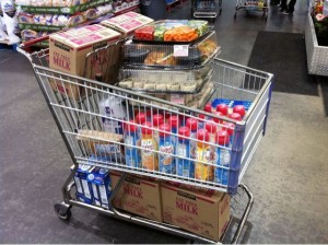 shopping cart filled with cases of milk, creamer, sugar, sandwiches, and veggies