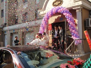 groom carries bride out of her house into waiting car as confetti rains down