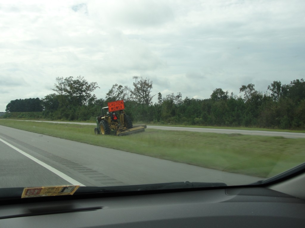 lawn mower vehicle driving along side of freeway mowing grass