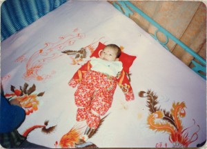 chinese baby wrapped in poufy red swaddling clothes laying on bed
