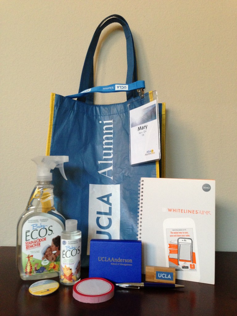 ucla alumni day swag including bag & button, ecos products, whitelines notebook, ucla anderson items, raytheon notepad, and wooden usb