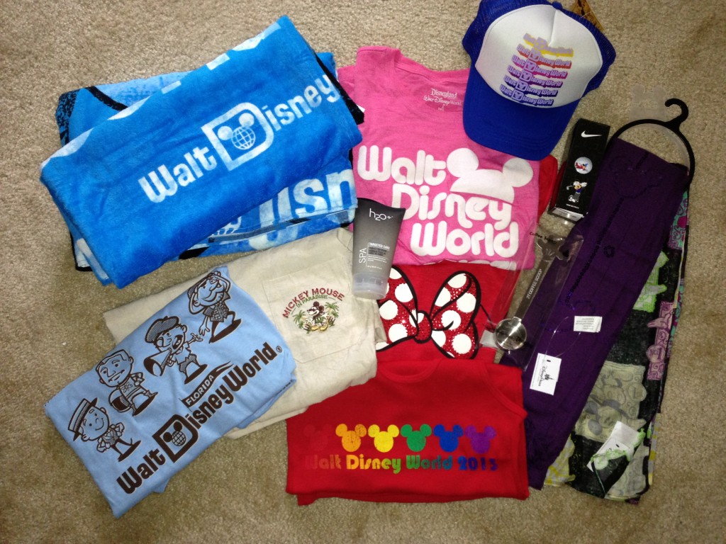 disney products laid out including beach towels, tshirts, trucker hat, tank tops, scarves, coffee scoop, foot scrub, and golf balls