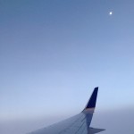 tip of airplane wing against horizon with bright moon in background