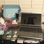 desk covered with laptop, boxes, and other items