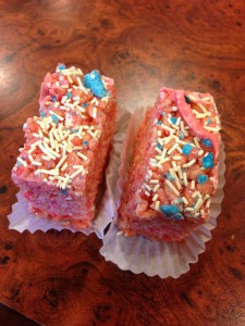 rice crispy treats dyed reddish pink topped with white sprinkles and blue sugar bits