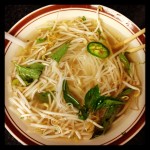 bowl of vietnamese pho noodles with basil leaves, bean sprouts, and jalapenos