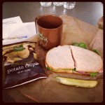 panera bread sandwich and pickle with side of potato chips