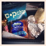 snacks on plane for united flight from us to uk including twix bar, popchips bag, bag of baby carrots, and burrito