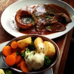 plate of traditional british sunday roast with roast beef and gravy, yorkshire pudding, potatoes, broccoli, and carrots