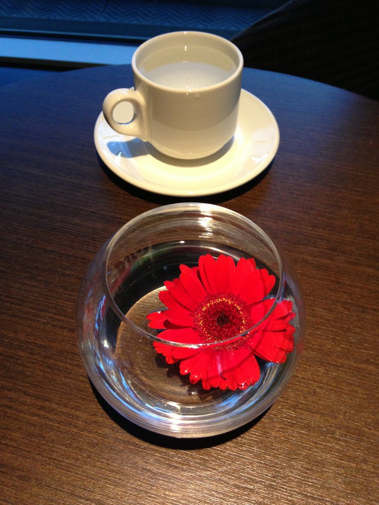 red flower floating in water as centerpiece with mug of water on table
