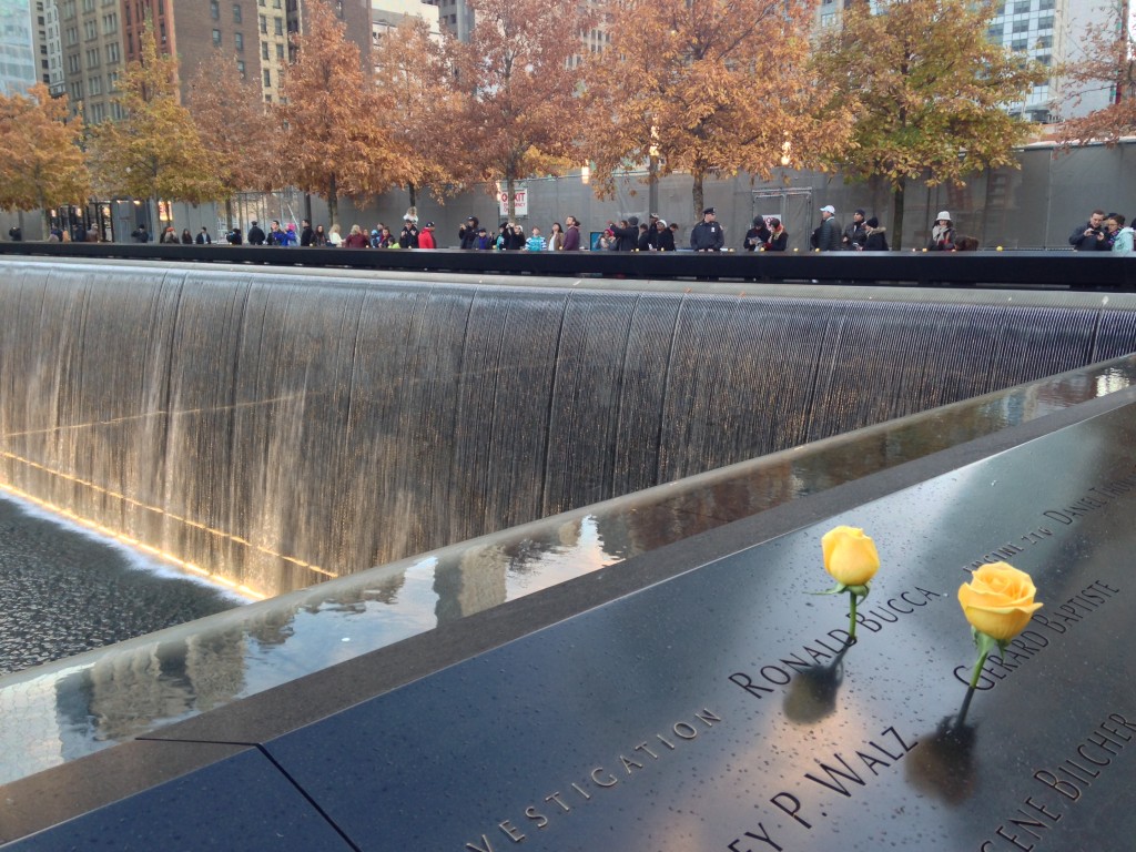 9/11 memorial falling water with yellow roses on names and people lined up looking out