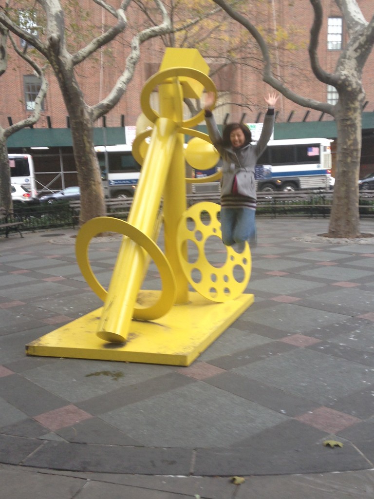 jumping off of and next to giant yellow sculpture in small park in new york city