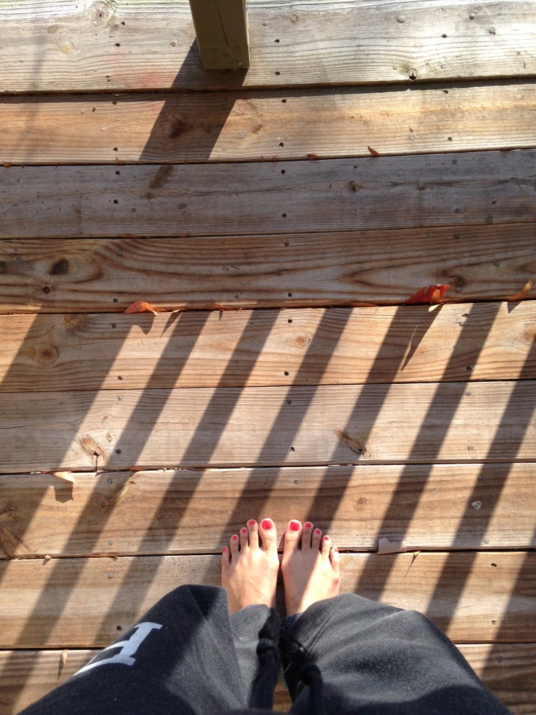 barefoot on porch in sunlight with shadows of railing