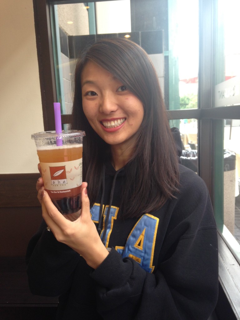 girl smiling holding up cha for tea peach iced tea drink with boba