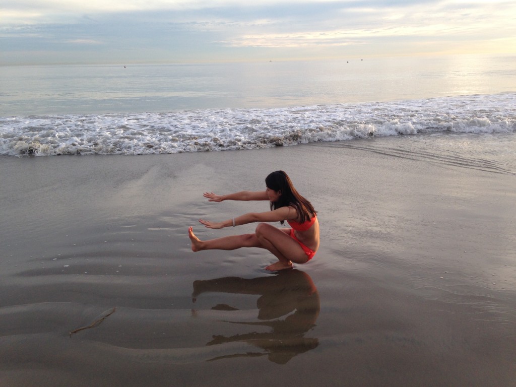 girl in orange bikini doing pistol exercise on sand at beach