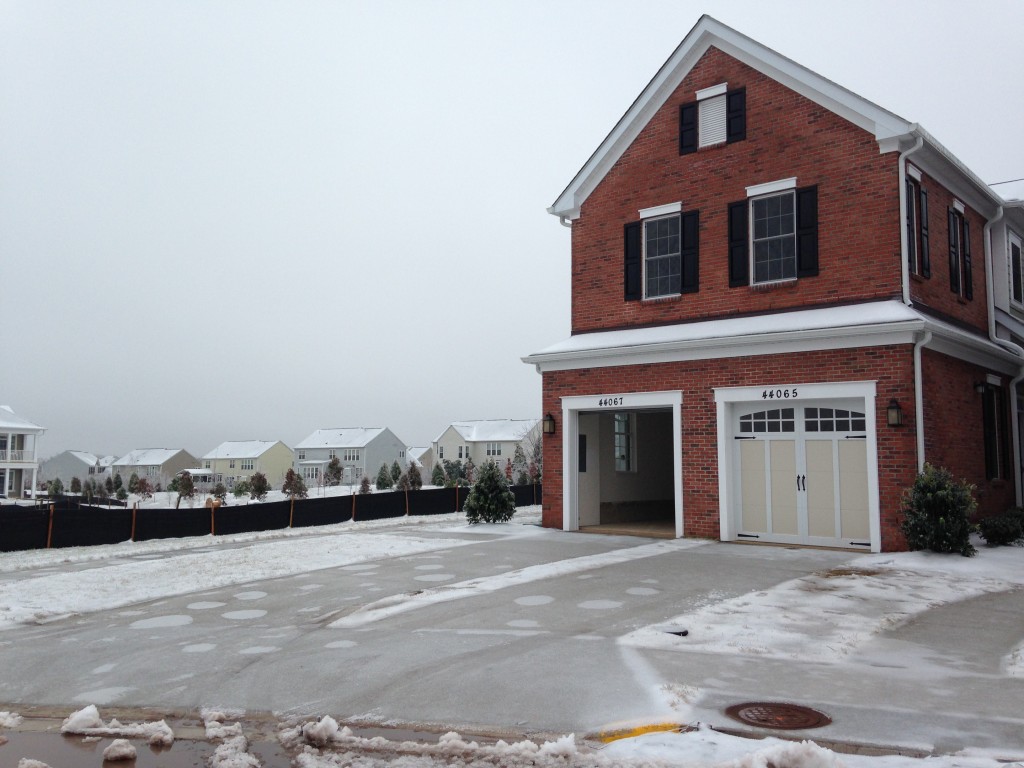 front of new condo with frozen driveway, one garage door open and one closed, and brick facade