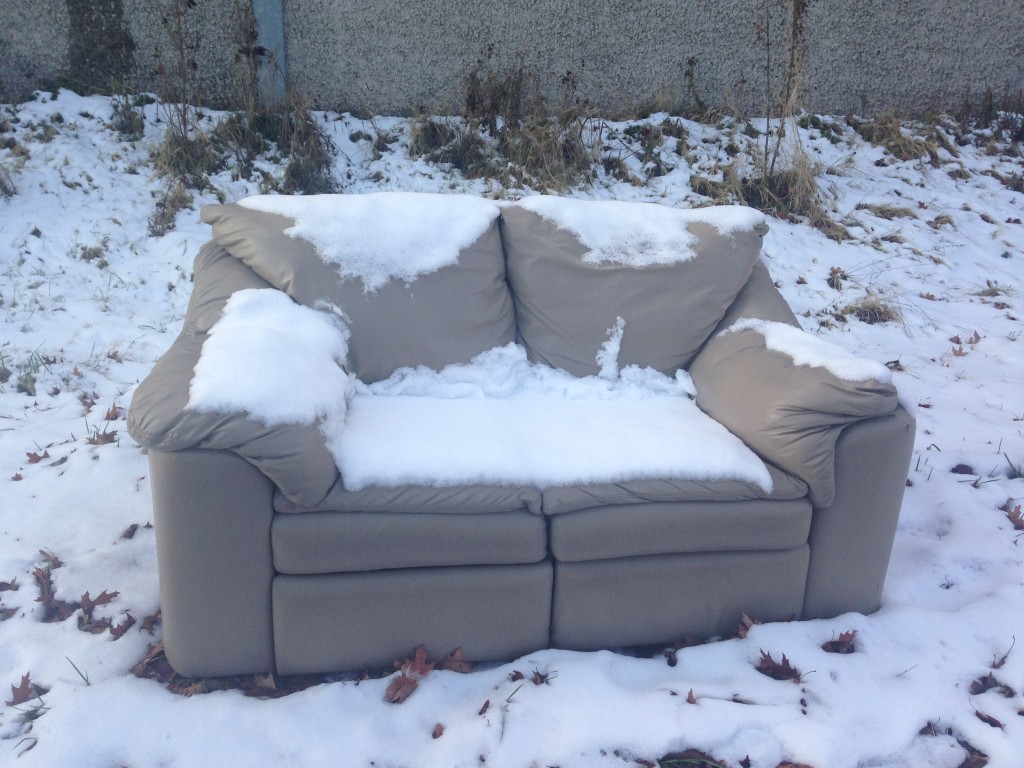 sofa sitting by side of road covered in snow from storm