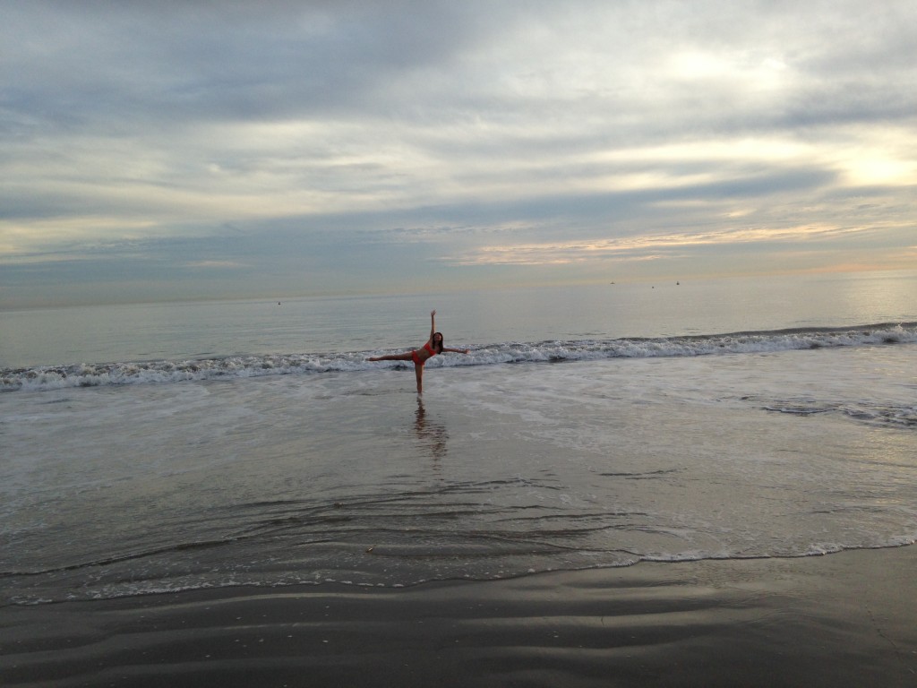 girl standing in ocean at beach stretching arms and legs out like starfish