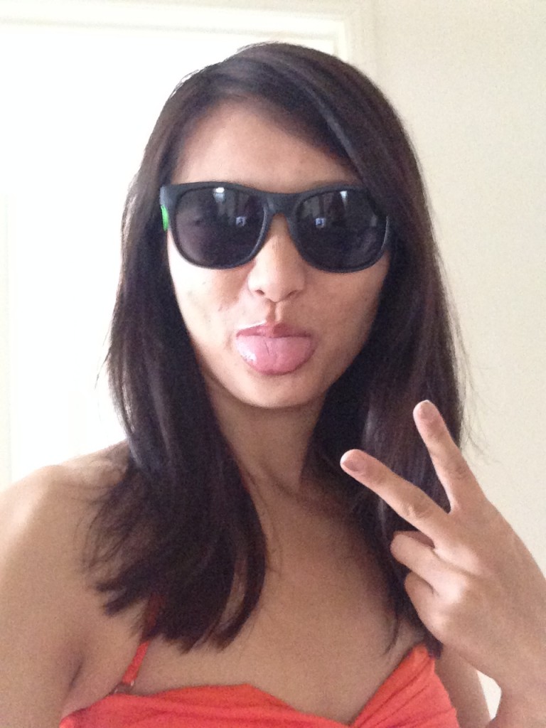girl wearing cheap plastic sunglasses and orange bikini top holding up peace sign and sticking out tongue