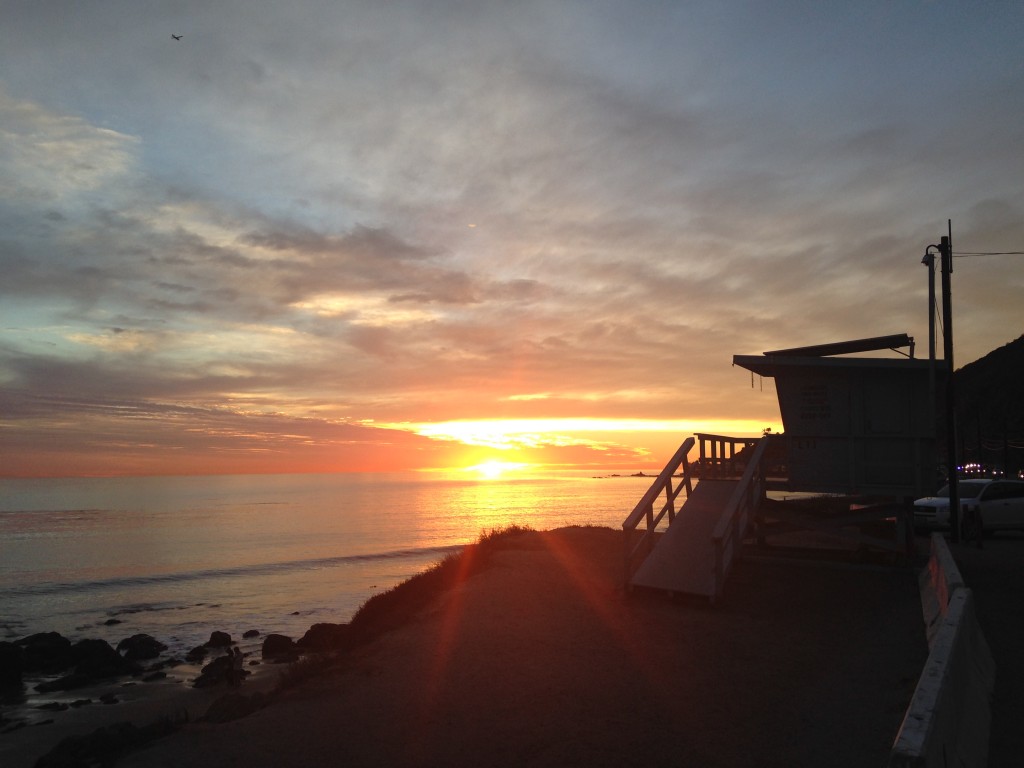 view of sunset from side of road by beach with lifeguard station silhouette