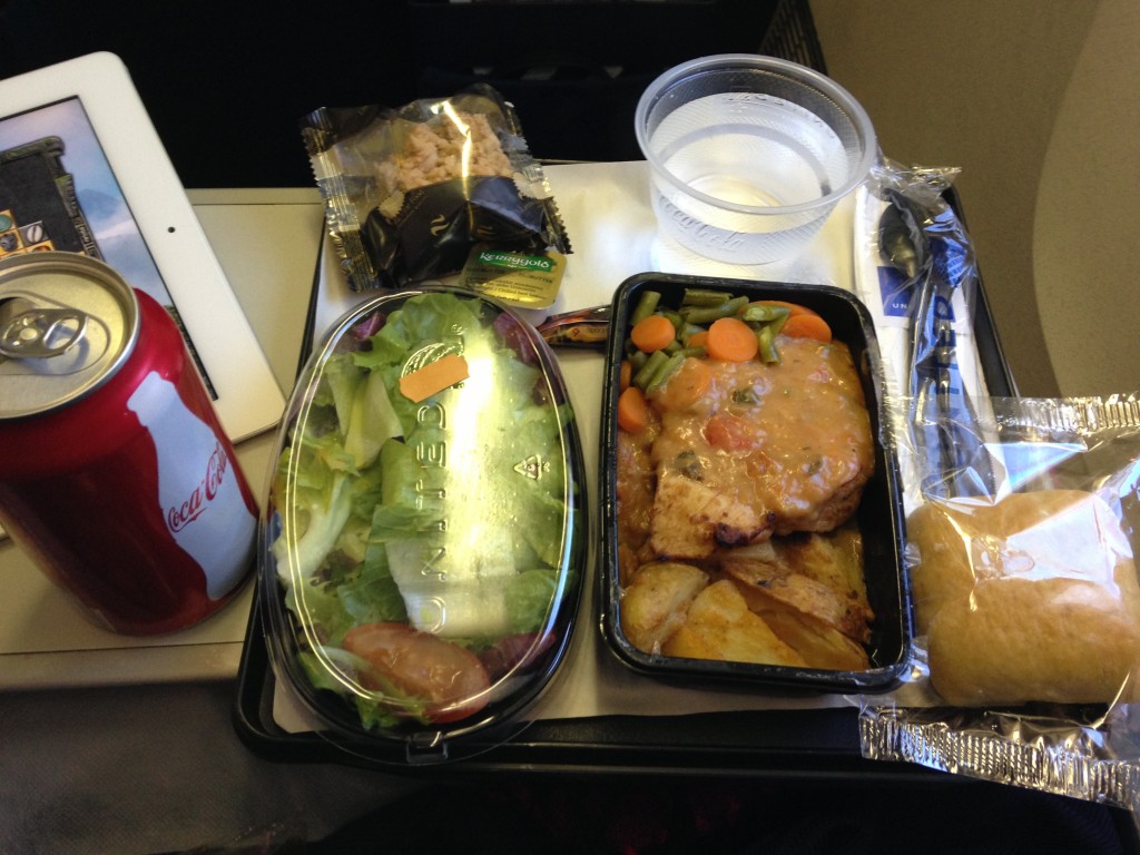 airplane meal with coca-cola soda, salad, chicken and vegetables, potato side, bread, and water