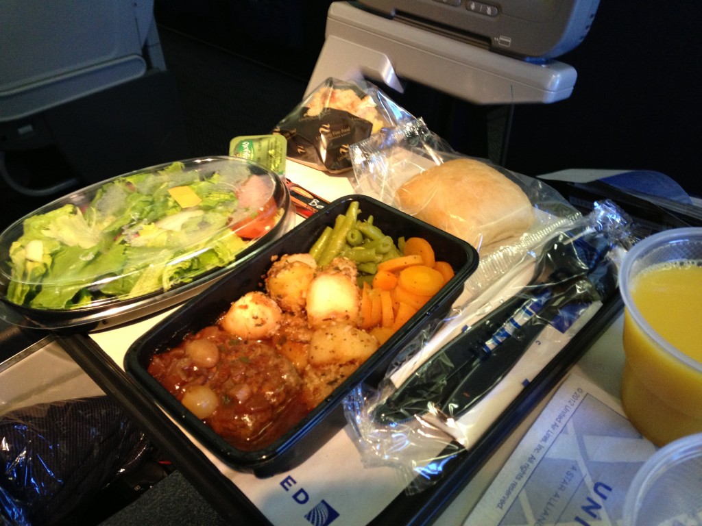 airplane meal with salad, beef and vegetables, bread, and orange juice