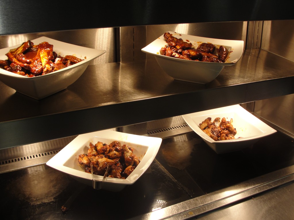 bowls of chicken wings and pork ribs under heat lamps