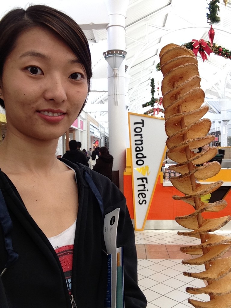 girl holding giant stick of tornado fries in front of kiosk in mall