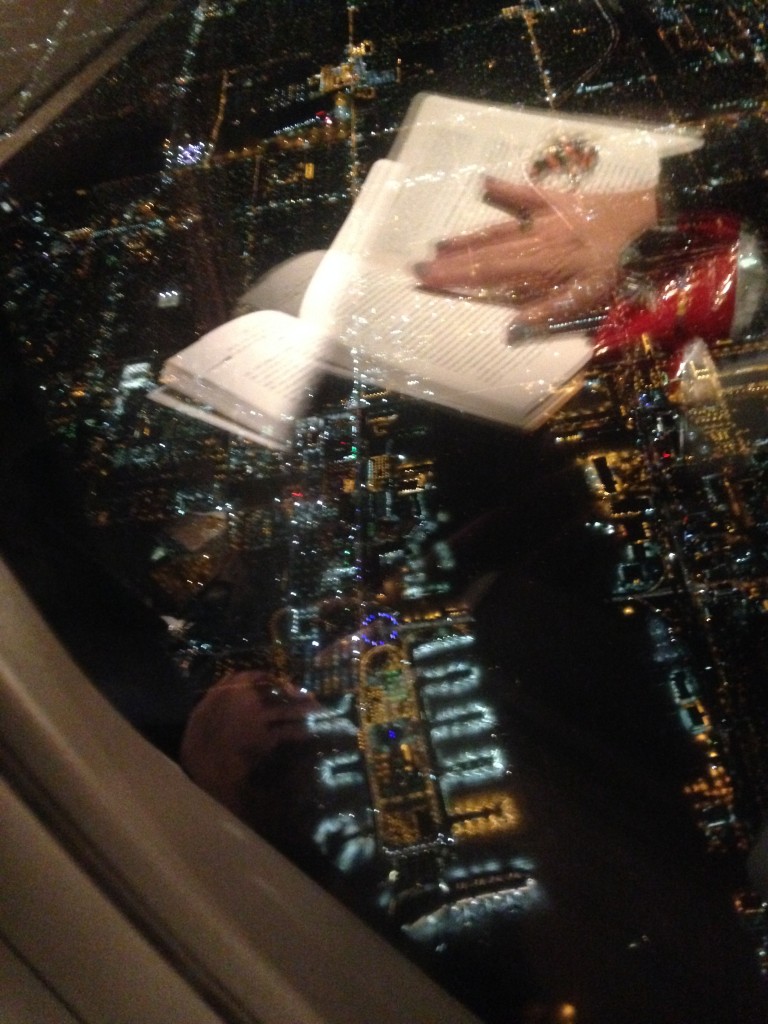 view of lax airport at night from airplane window with reflection of book and person's hand
