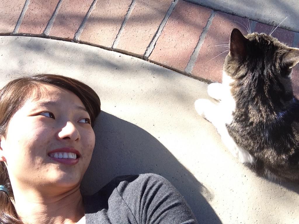 girl laying on ground looking over and smiling at cat looking into distance
