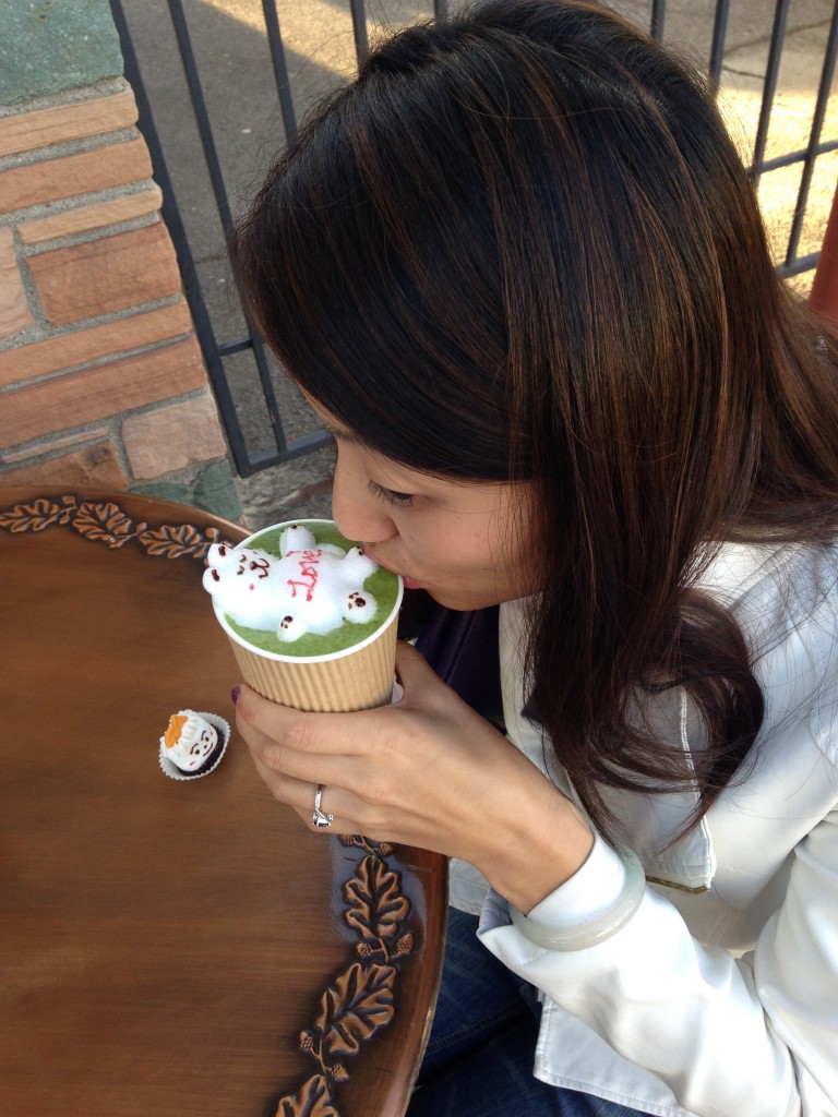 girl sipping japanese matcha green tea latte with 3d latte art of bear at outdoor table of cafe