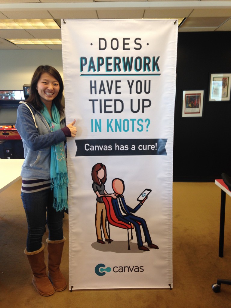 girl holding thumbs up standing next to canvas vertical banner with "does paperwork have you tied up in knots? canvas has a cure!" messaging