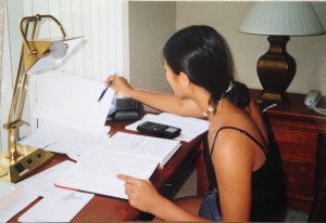 girl sitting at hotel desk studying with textbook, homework, and graphing calculator