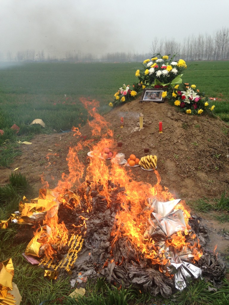 giant pile of paper money burning in front of dirt mound grave site