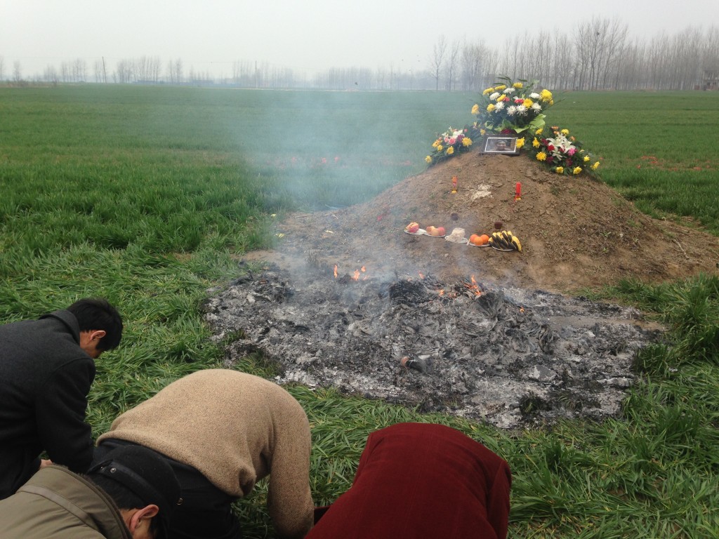 kow towing at grave site with smouldering ashes of burning paper