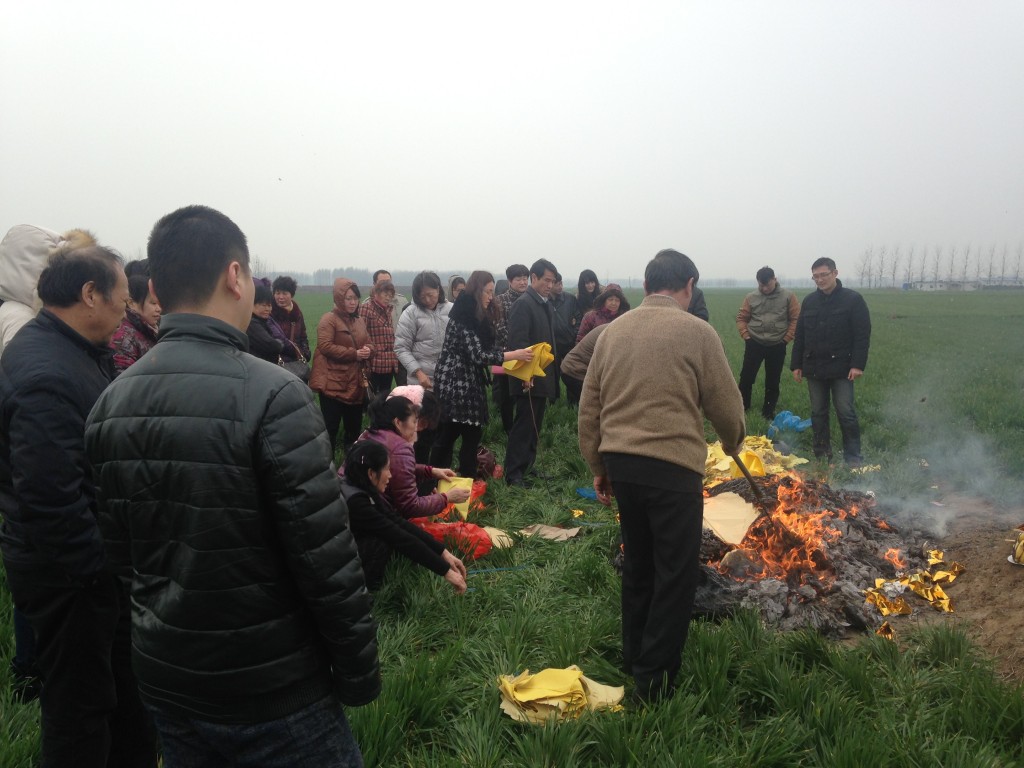 stoking large pile of burning paper at grave site