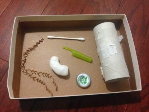 box with paper scraps, packing peanut, q-tip, pen cap, bottle cap, and toilet paper tube that make great free cat toys