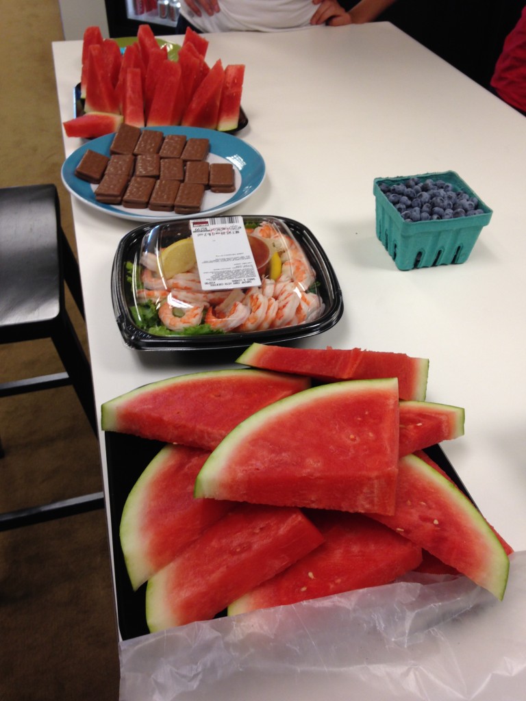 watermelon, blueberries, cocktail shrimp, and tim tams spread out on table for office happy hour