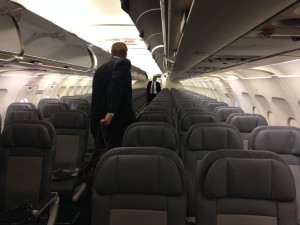 rows of empty seats on plane as first people start boarding and flight attendant waits near back