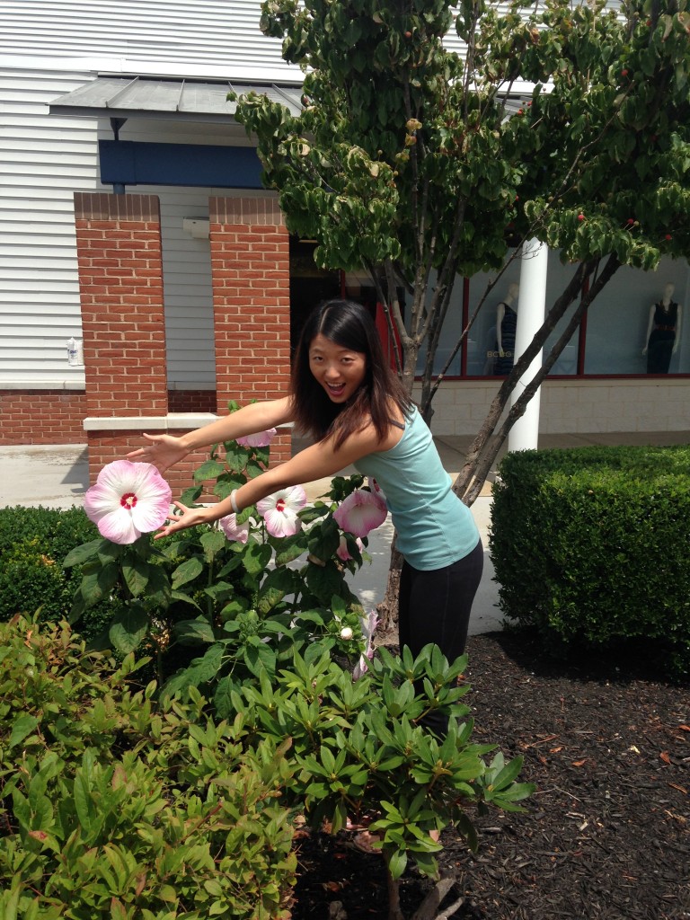girl stretching hands out towards giant hibiscus flower larger than both hands
