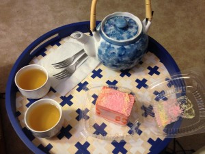 blue and white tea pot, tea cups with tea in them, and slice of strawberry cake on round wooden tray