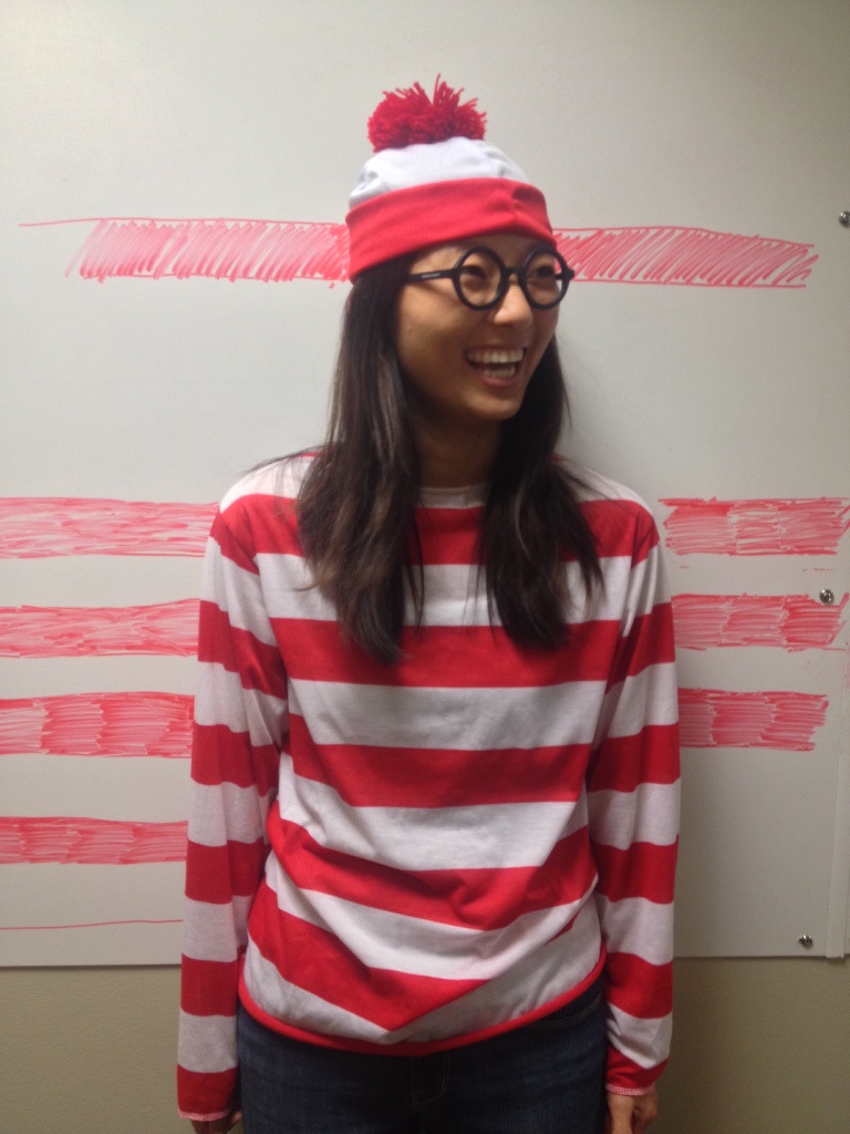 laughing girl dressed up as waldo for halloween blending in with whiteboard with red stripes drawn on