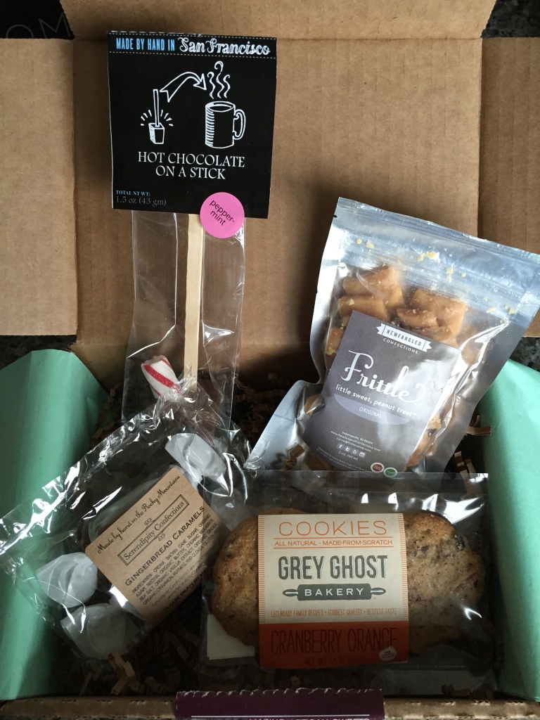 treatsie december 2014 box contents with ticket chocolate hot chocolate on a stick, newfangled confections frittle, serendipity confections caramels, and grey ghost bakery cookies