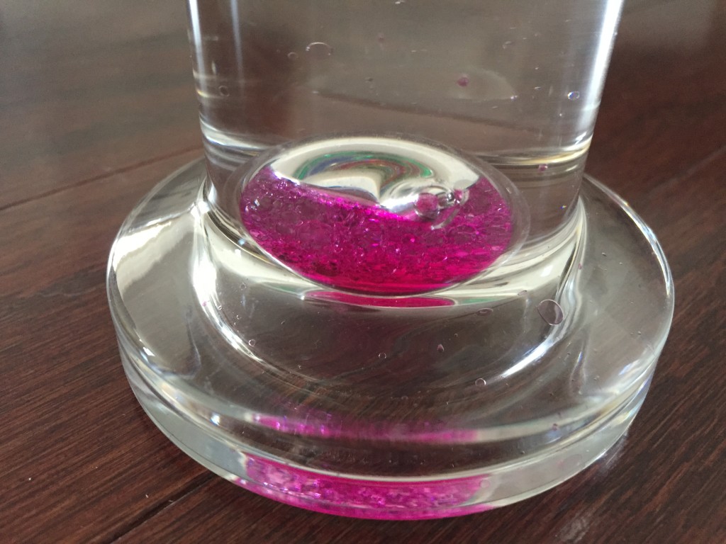 bottom of galileo thermometer with pink temperature globe laying leaking