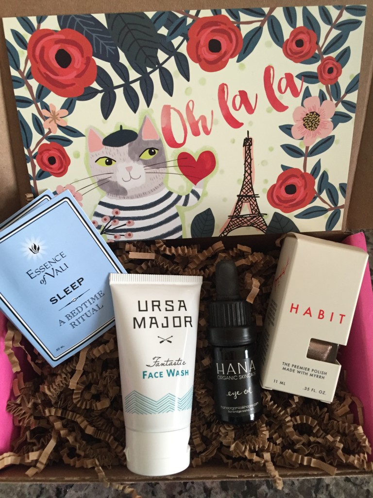 contents of petit vour october 2015 box with essence of vali essential oil, ursa major face wash, hana eye oil, habit nail polish, and info card with oh la la theme