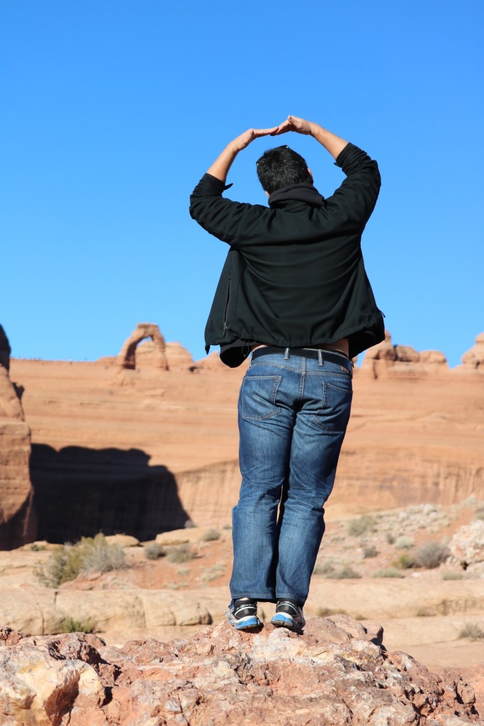 standing with arms outstretched overhead with delicate arch in the background